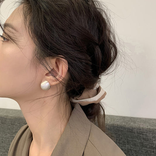 Close-up of brushed dome-shaped silver earrings with a matte finish from STUD, displayed on a white cloth backdrop.