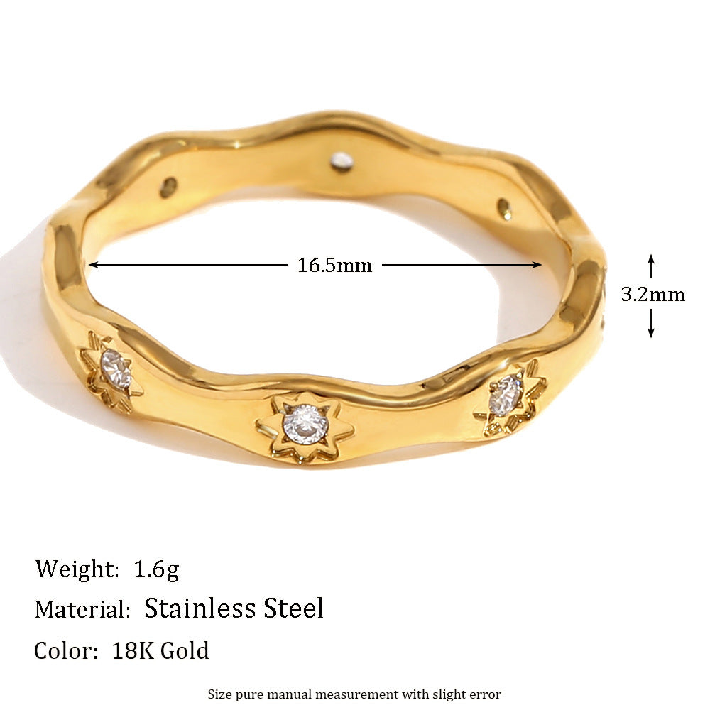 Gold wavy ring with engraved 8-point star motifs and zircon stones on a cream textured background