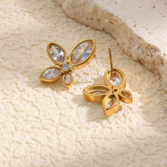Gold marquised-shaped earrings with clear gemstones on a beige stone background