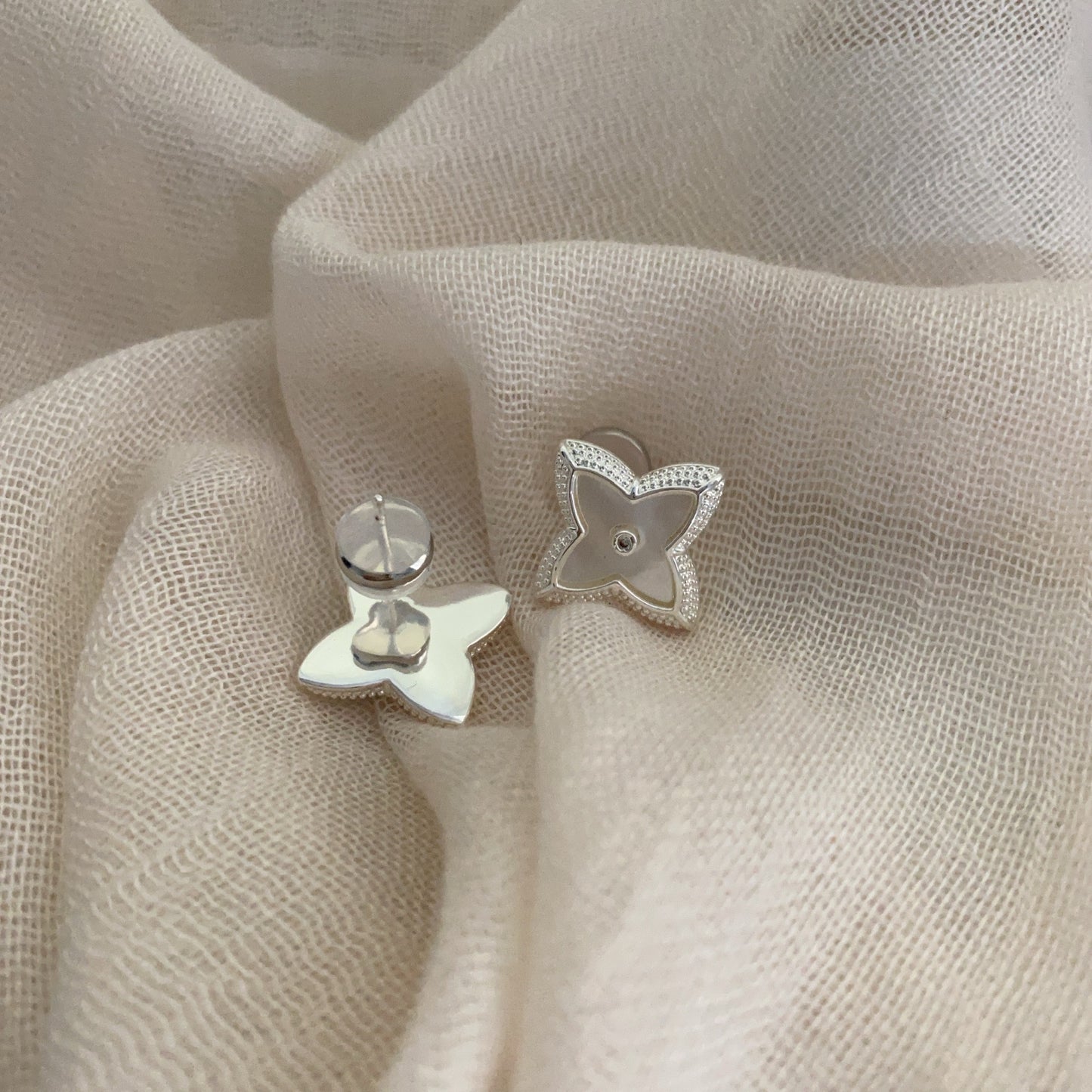 Close-up of white shell four-leaf clover stud earrings with zircon border by STUD on wooden background