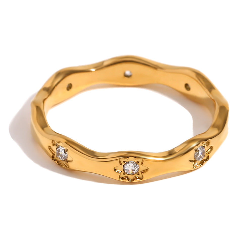 Gold wavy ring with engraved 8-point star motifs and zircon stones on a cream textured background
