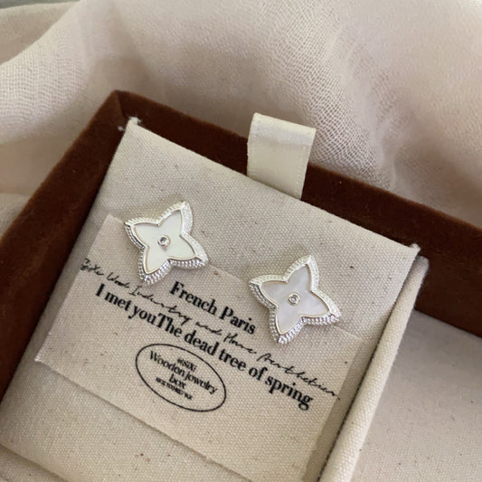 Close-up of white shell four-leaf clover stud earrings with zircon border by STUD on wooden background