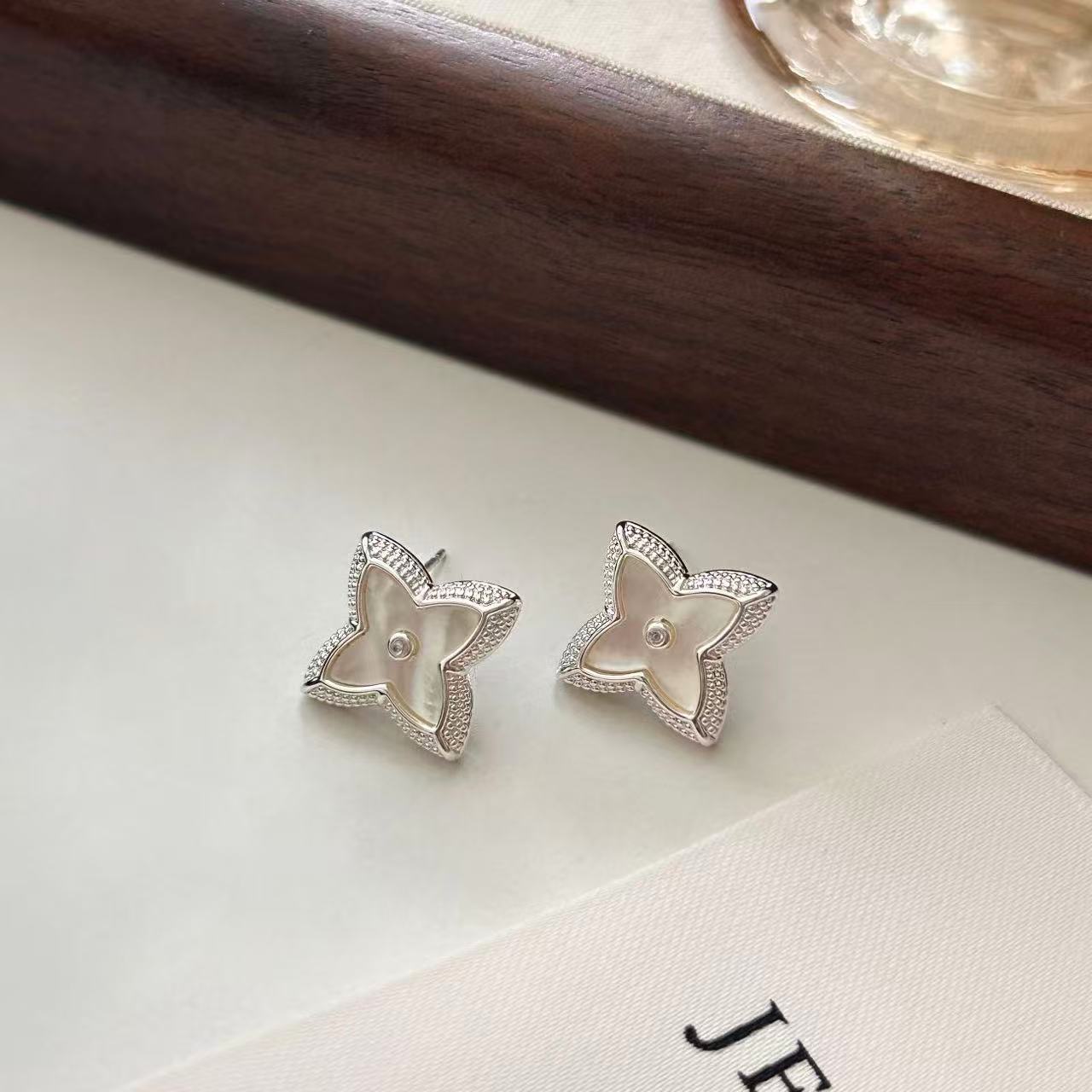Close-up of white shell four-leaf clover stud earrings with zircon border by STUD on wooden background