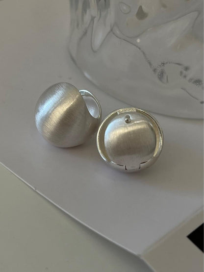 Close-up of brushed dome-shaped silver earrings with a matte finish from STUD, displayed on a white cloth backdrop.