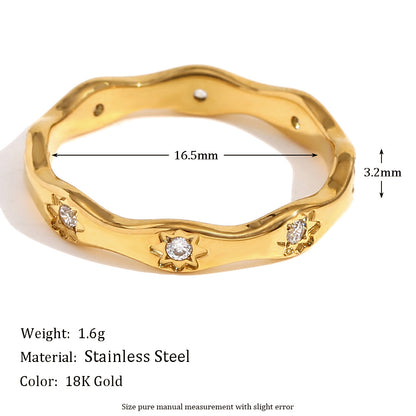 Gold wavy ring with engraved 8-point star motifs and zircon stones on a cream textured background