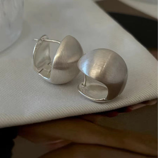 Close-up of brushed dome-shaped silver earrings with a matte finish from STUD, displayed on a white cloth backdrop.