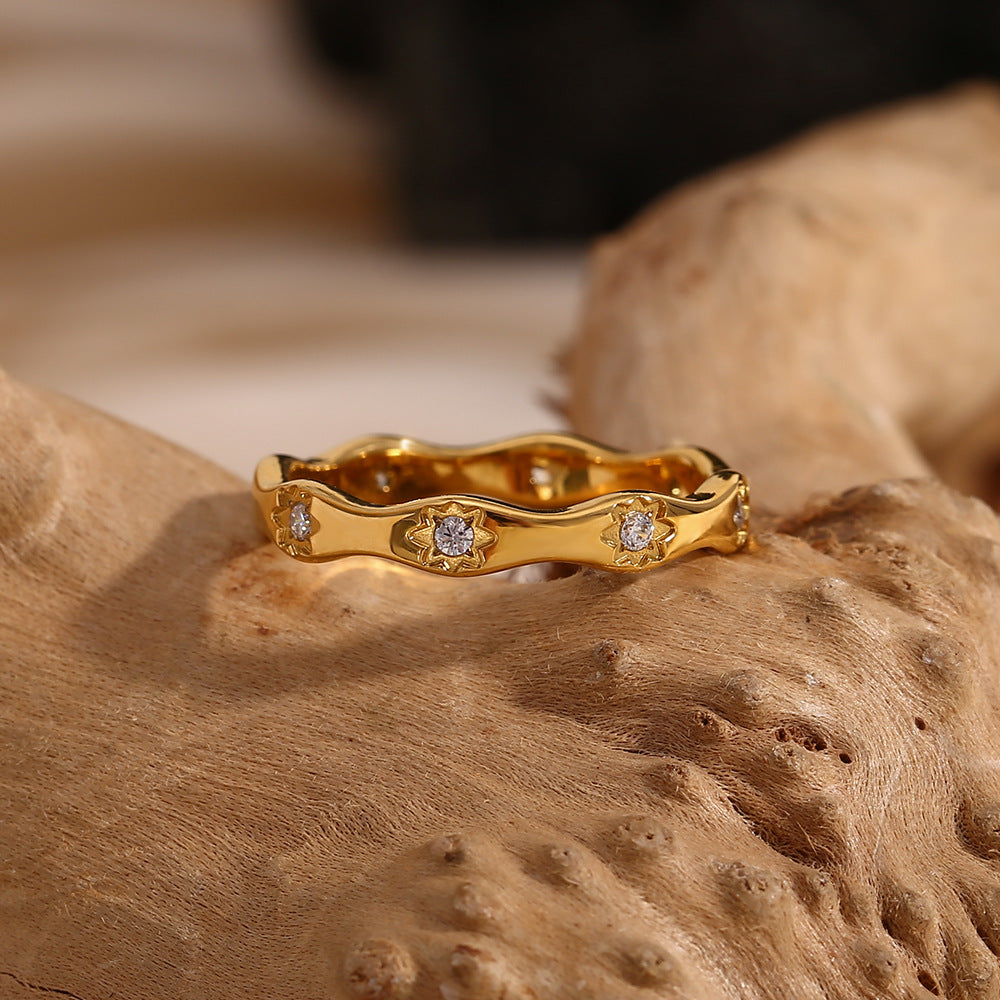 Gold wavy ring with engraved 8-point star motifs and zircon stones on a cream textured background