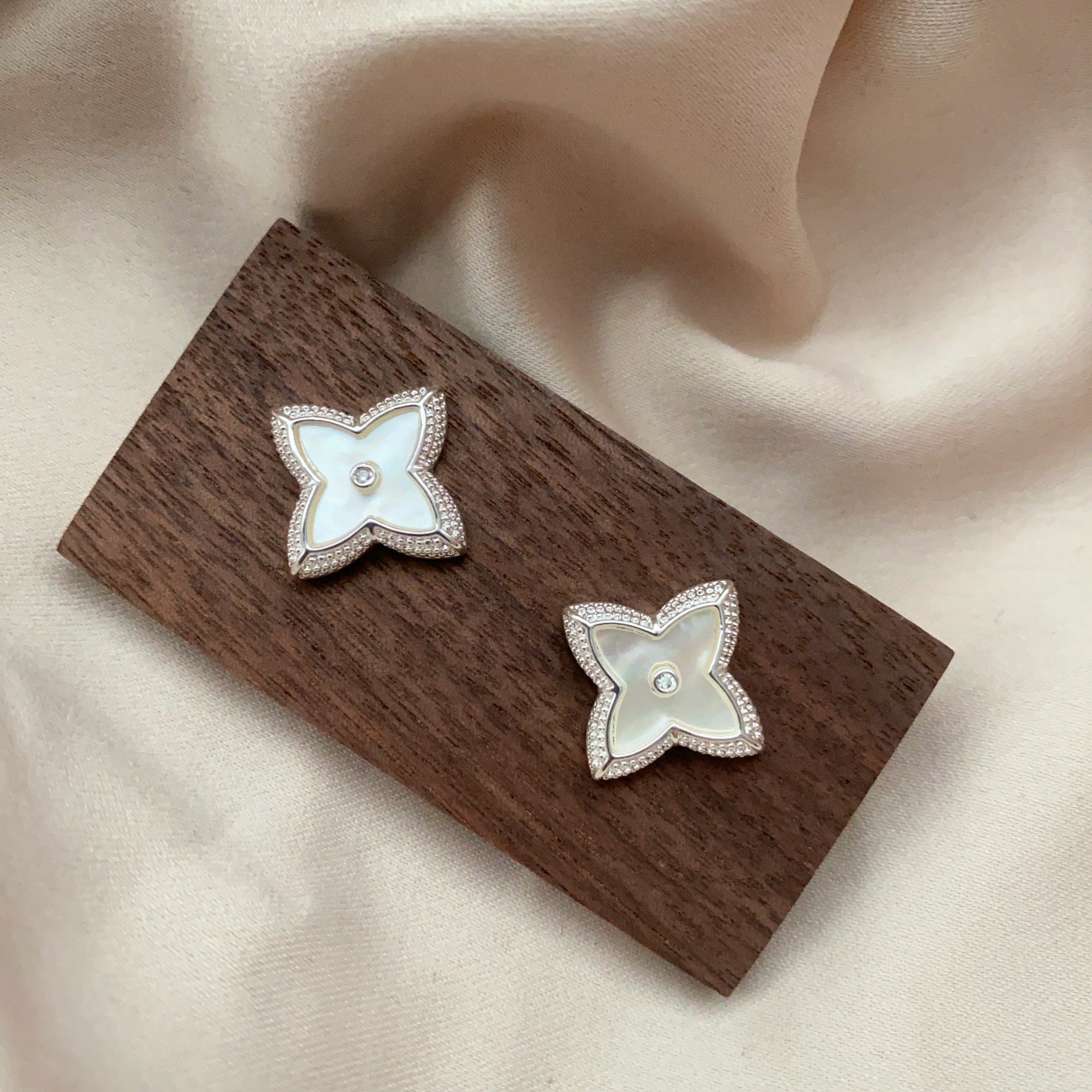 Close-up of white shell four-leaf clover stud earrings with zircon border by STUD on wooden background