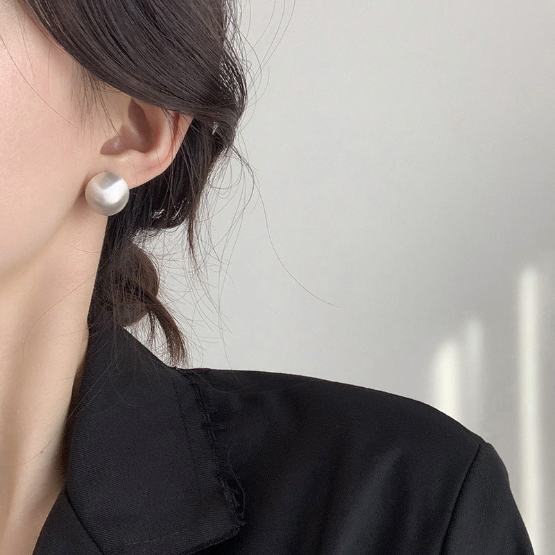 Close-up of brushed dome-shaped silver earrings with a matte finish from STUD, displayed on a white cloth backdrop.