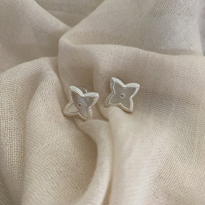 Close-up of white shell four-leaf clover stud earrings with zircon border by STUD on wooden background
