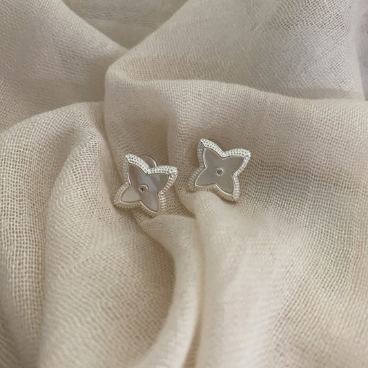 Close-up of white shell four-leaf clover stud earrings with zircon border by STUD on wooden background