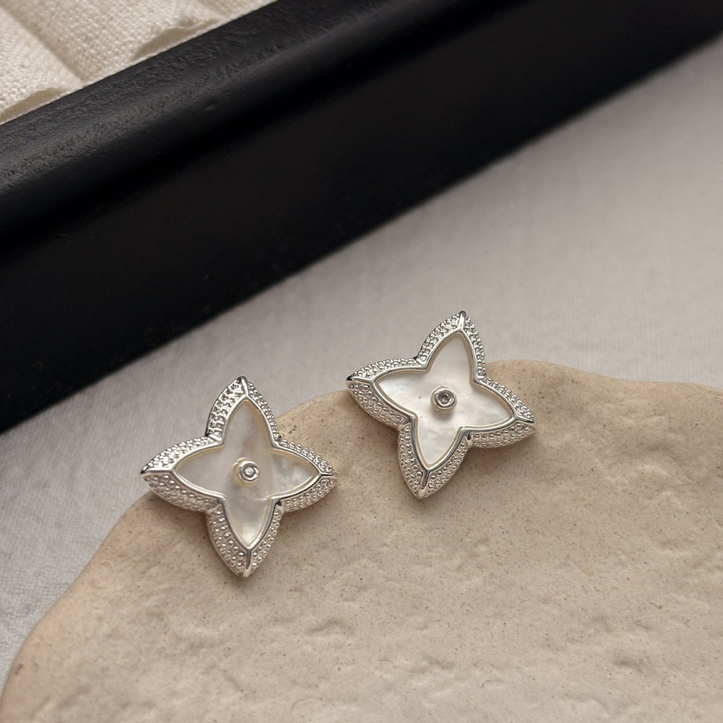 Close-up of white shell four-leaf clover stud earrings with zircon border by STUD on wooden background