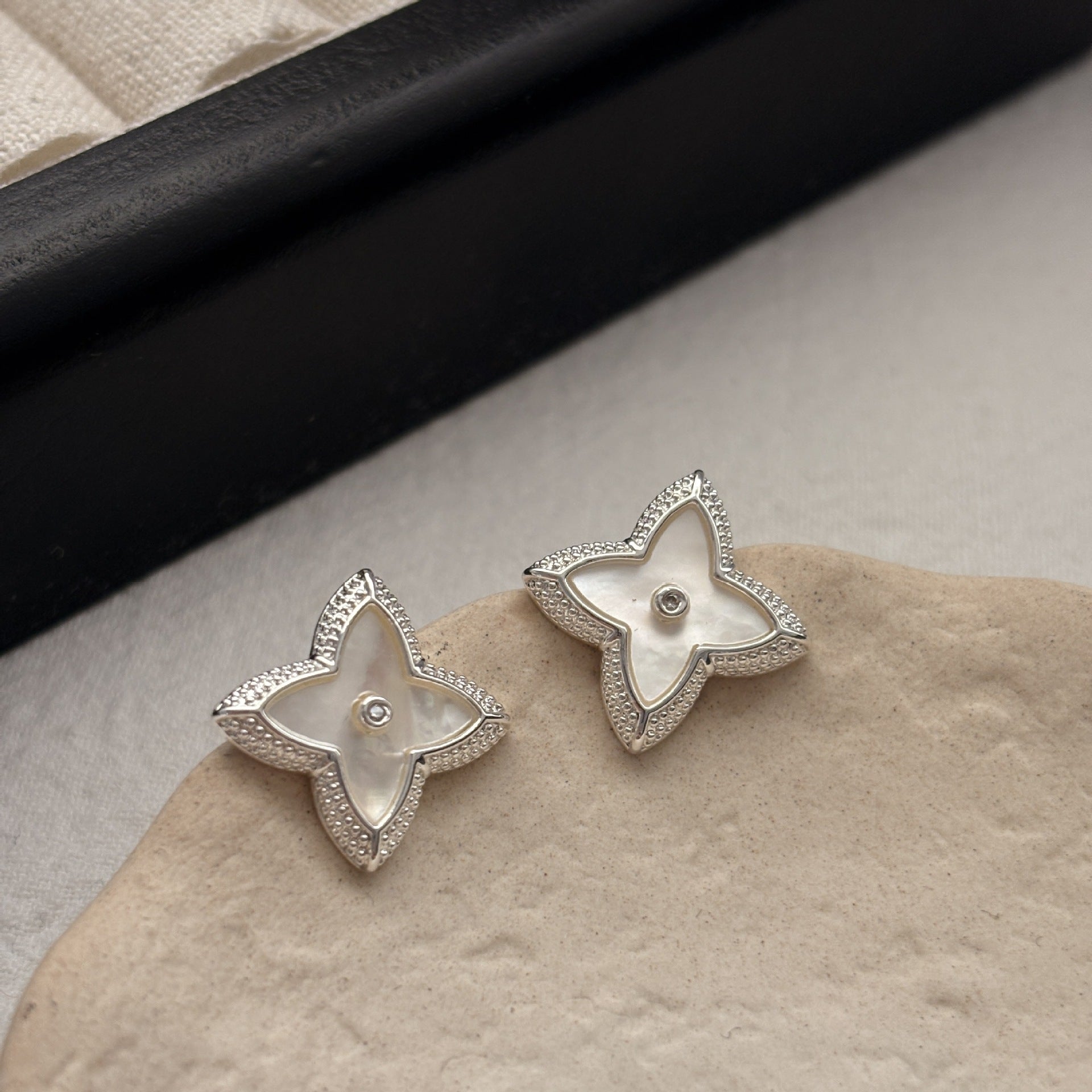 Close-up of white shell four-leaf clover stud earrings with zircon border by STUD on wooden background