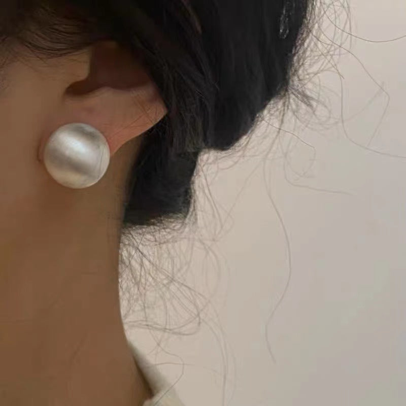 Close-up of brushed dome-shaped silver earrings with a matte finish from STUD, displayed on a white cloth backdrop.