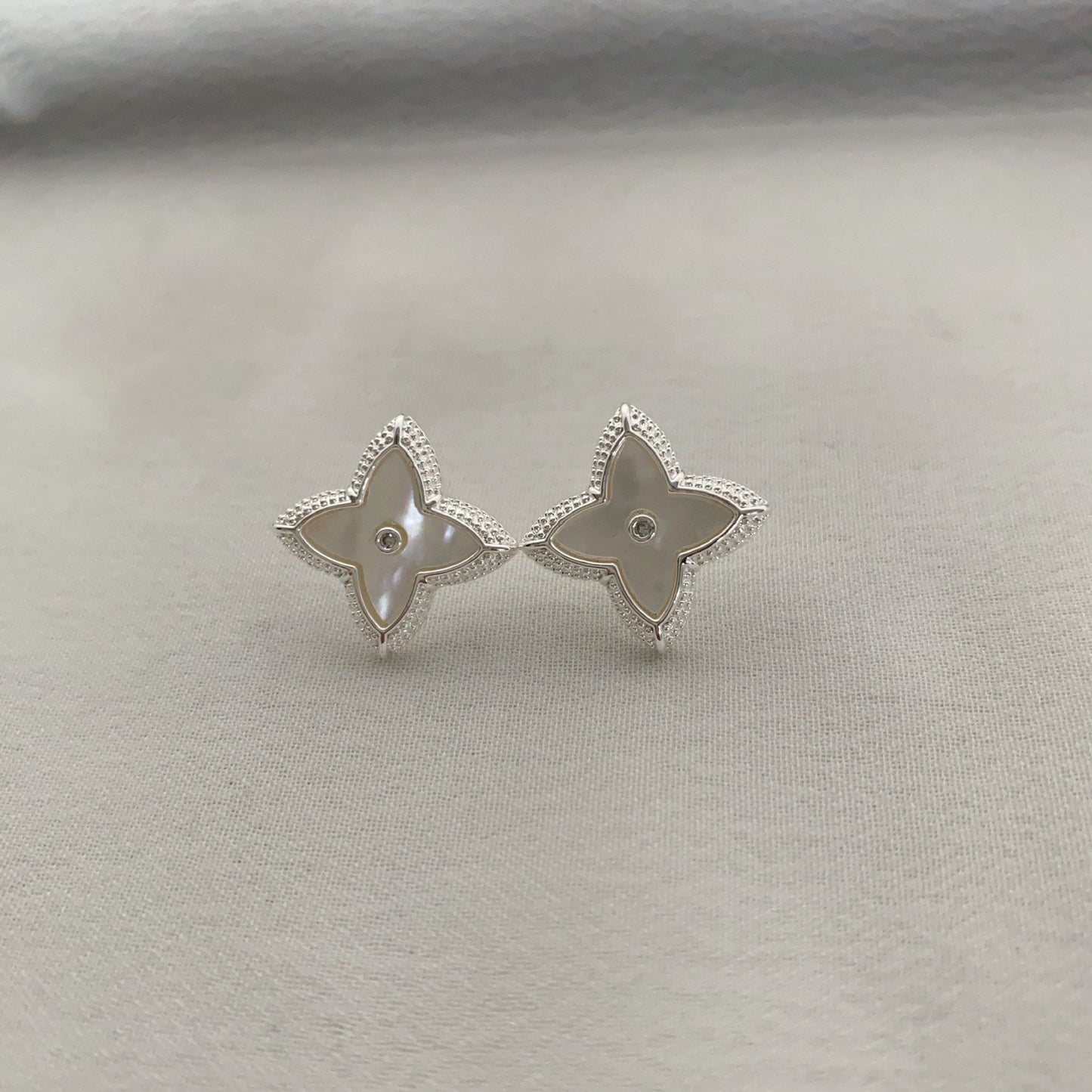 Close-up of white shell four-leaf clover stud earrings with zircon border by STUD on wooden background