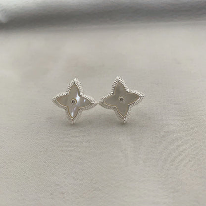 Close-up of white shell four-leaf clover stud earrings with zircon border by STUD on wooden background