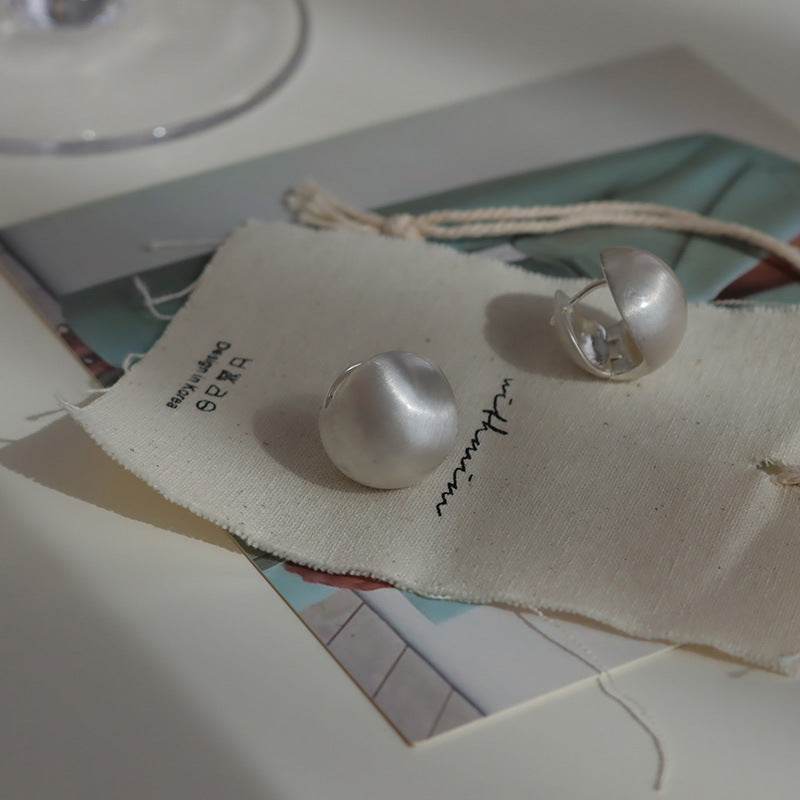 Close-up of brushed dome-shaped silver earrings with a matte finish from STUD, displayed on a white cloth backdrop.