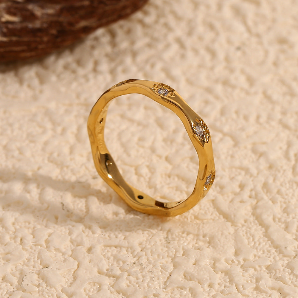 Gold wavy ring with engraved 8-point star motifs and zircon stones on a cream textured background