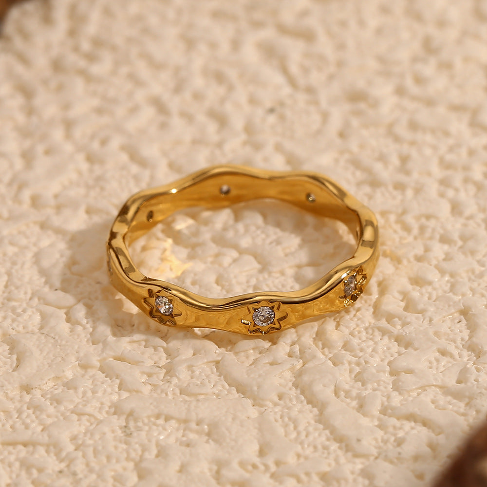 Gold wavy ring with engraved 8-point star motifs and zircon stones on a cream textured background