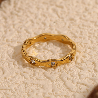Gold wavy ring with engraved 8-point star motifs and zircon stones on a cream textured background