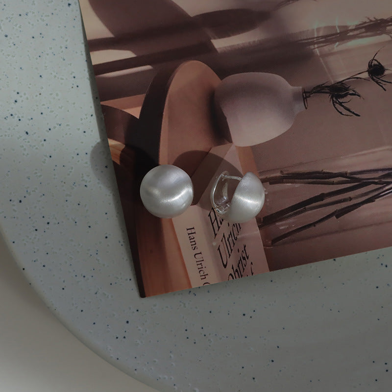Close-up of brushed dome-shaped silver earrings with a matte finish from STUD, displayed on a white cloth backdrop.