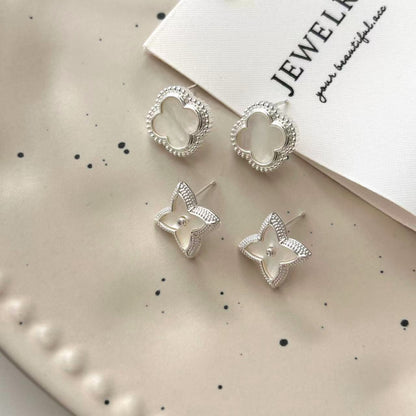 Close-up of white shell four-leaf clover stud earrings with zircon border by STUD on wooden background