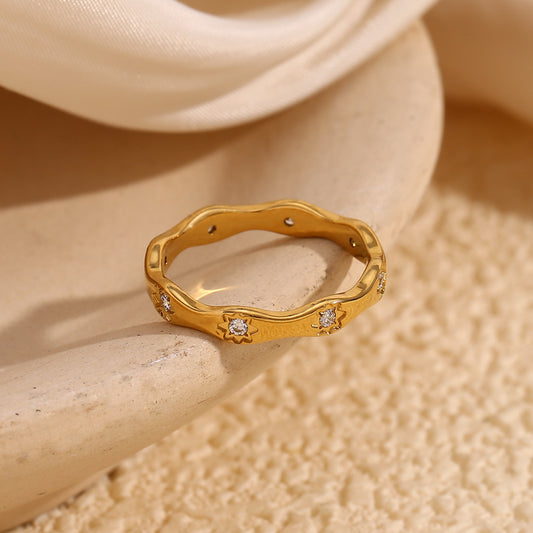 Gold wavy ring with engraved 8-point star motifs and zircon stones on a cream textured background