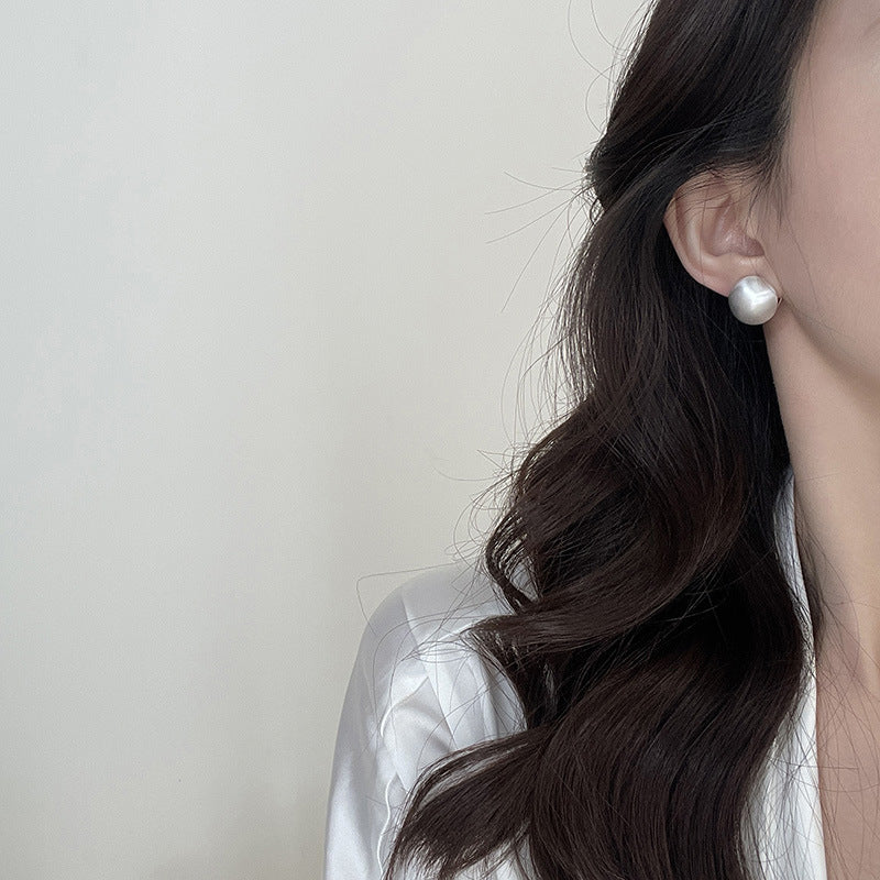 Close-up of brushed dome-shaped silver earrings with a matte finish from STUD, displayed on a white cloth backdrop.