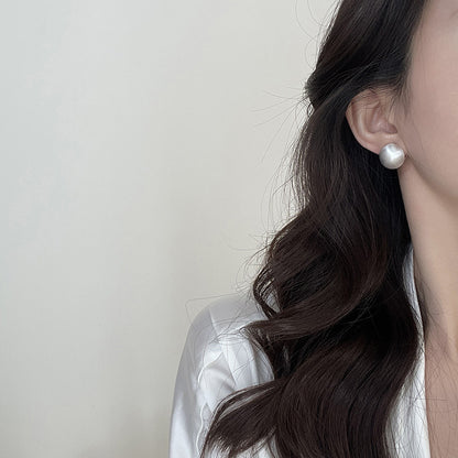 Close-up of brushed dome-shaped silver earrings with a matte finish from STUD, displayed on a white cloth backdrop.
