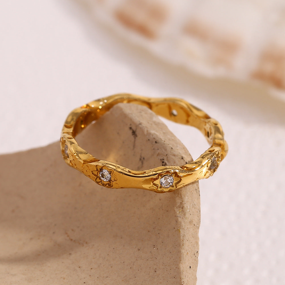 Gold wavy ring with engraved 8-point star motifs and zircon stones on a cream textured background