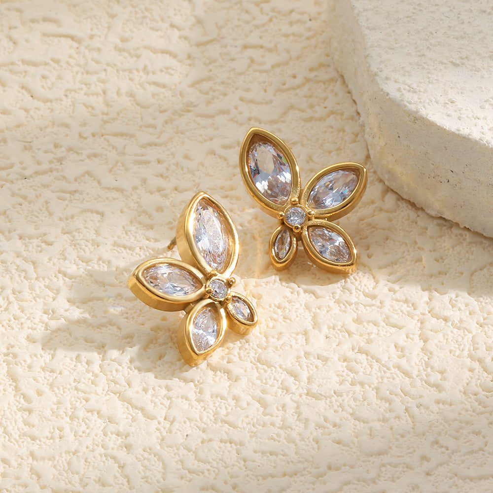Gold earrings with clear gemstones on a textured beige surface