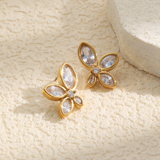 Gold earrings with clear gemstones on a textured beige surface
